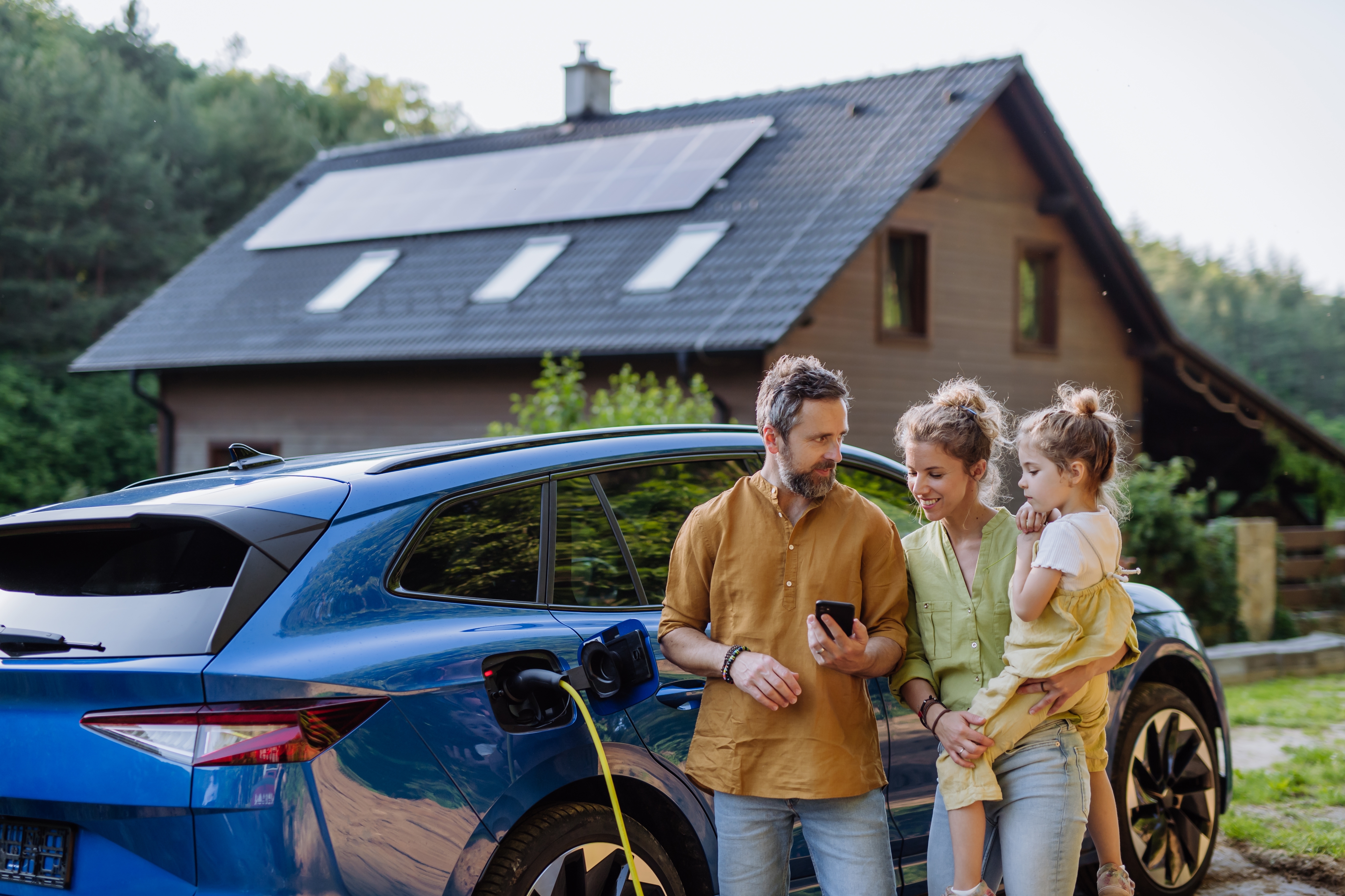 Young family stand beside car and in front of house
