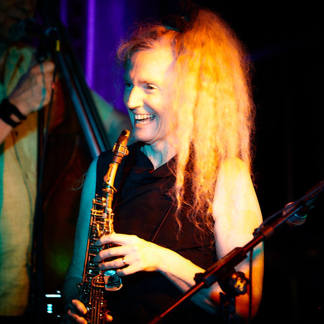 Sandy is in the middle of a performance, smiling with a saxophone in her hands.