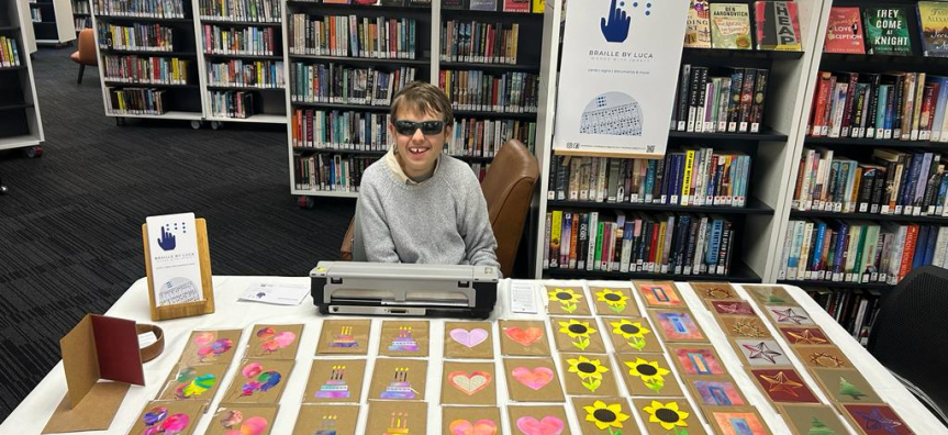 Luca Weber sitting behind a market stall table with an assortment of holiday cards laid out. 