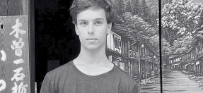 Photo of Enzo Munro, standing in front of a painted streetscape. 